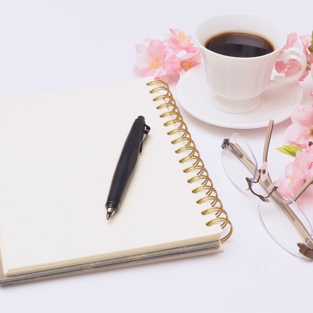 Notebook, coffee, reading glasses, and pink flowers arranged for a quiet everyday ritual.